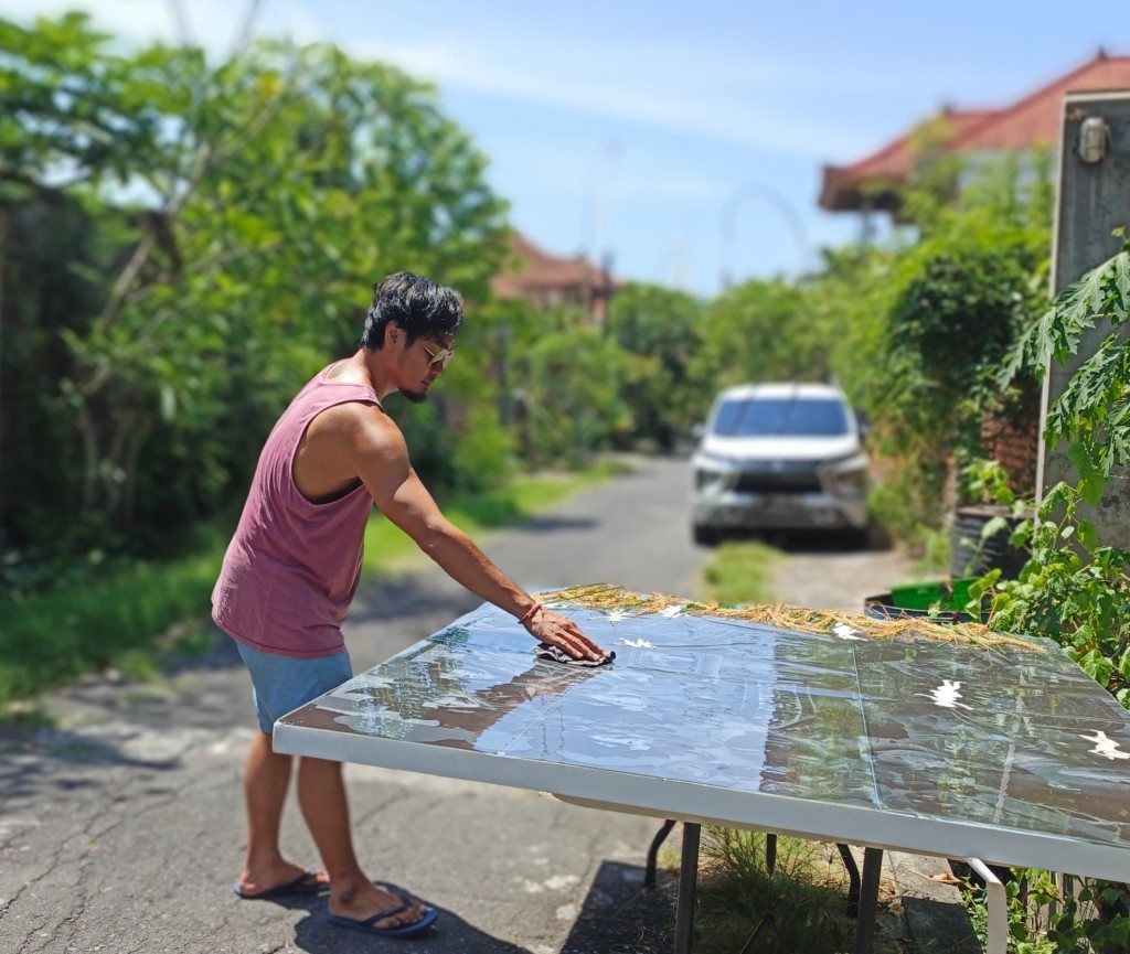 Budi Agung Kuswara exposing a cyanotype with an arrangement on padi rice and grass outdoors under the sun at his studio in Bali. Photo taken in 2025. Image courtesy of the artist. 